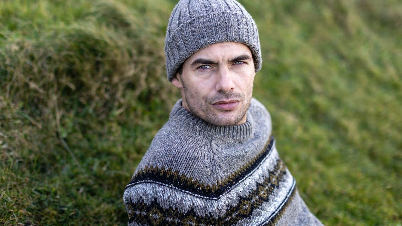 Man sitting on grass wearing a knitted jumper and cap