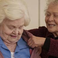 An old woman is helping another old woman put her coat on.