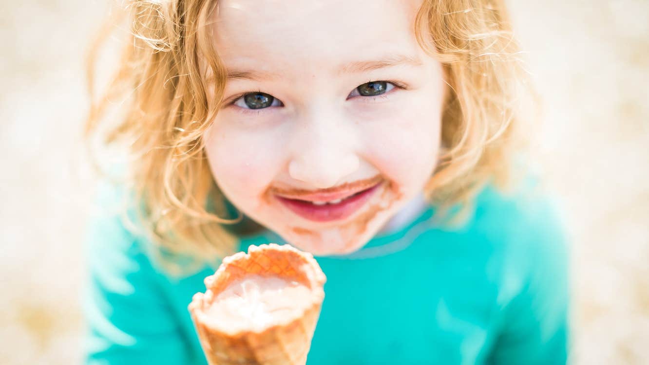 A smiling young girl enjoys ice cream from a cone
