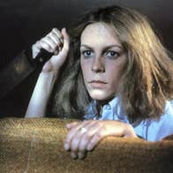 A woman with a kitchen knife is hiding behind a piece of furniture.