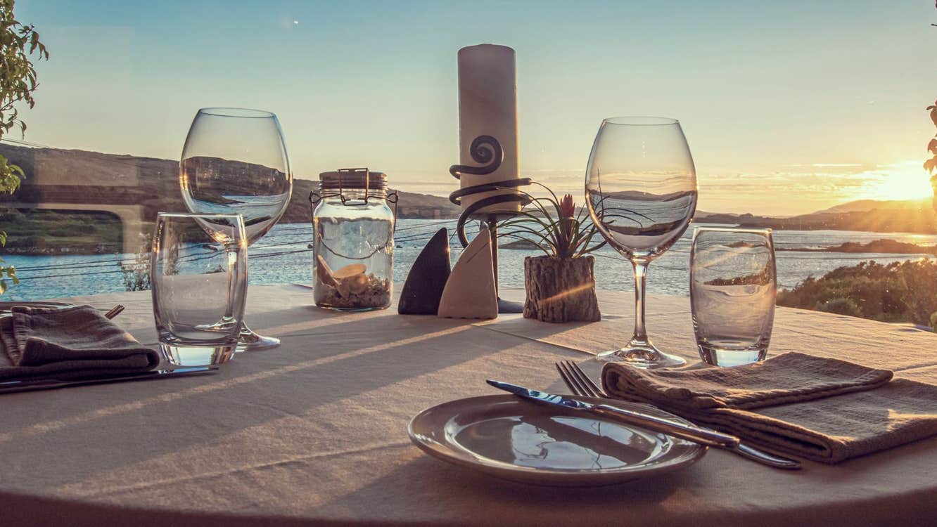 A set table with wine glasses and the sun setting in the background