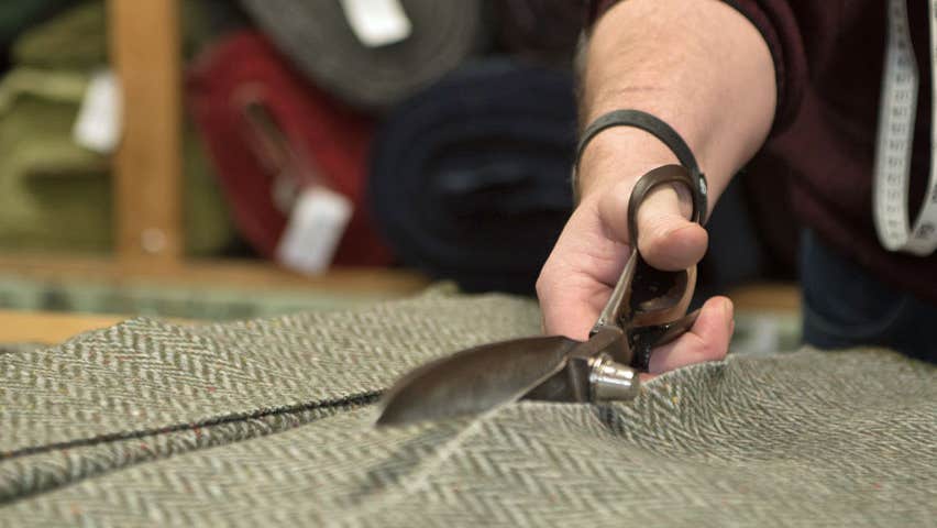 Image of person with a shears cutting through a piece of Donegal tweed
