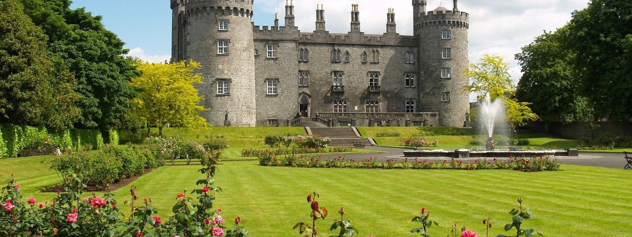A view of Kilkenny Castle with a border of red and pink roses in foreground