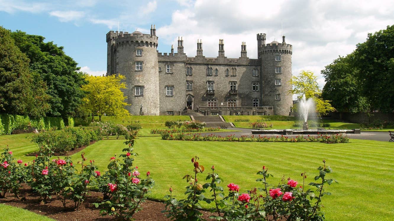 A view of Kilkenny Castle with a border of red and pink roses in foreground
