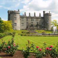 A view of Kilkenny Castle with a border of red and pink roses in foreground