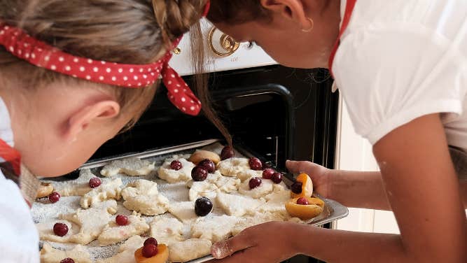 2 children are putting a tray of unbaked biscuits into an open oven.