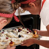 2 children are putting a tray of unbaked biscuits into an open oven.