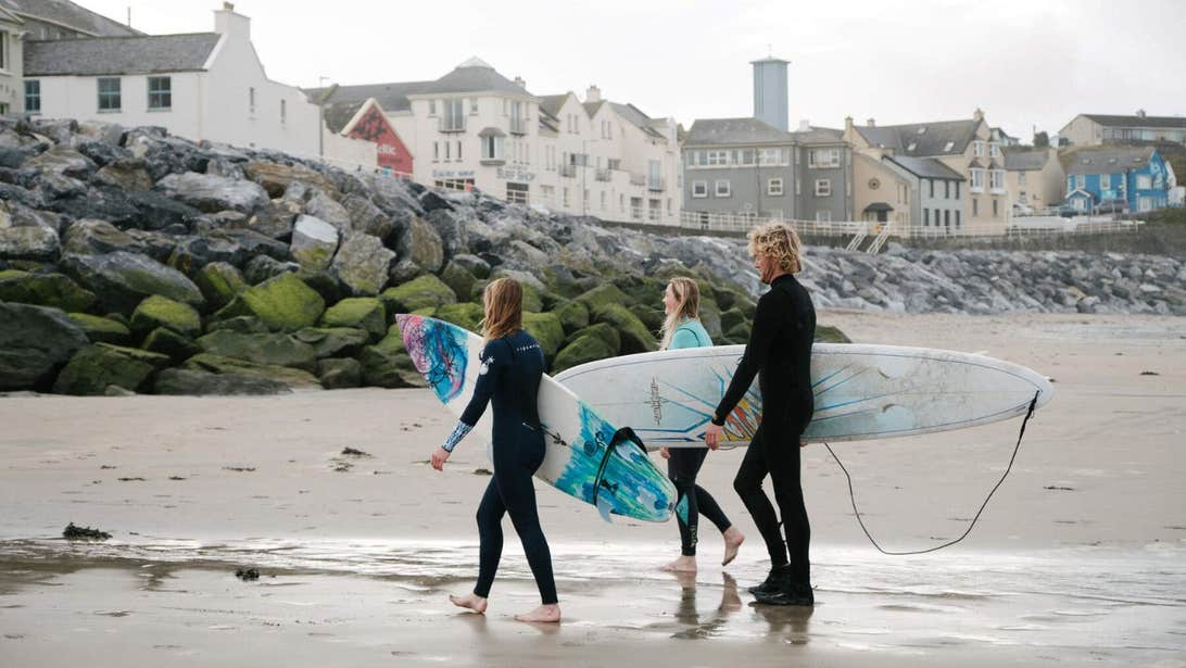Three surfers walking up the beach with their surfboards under their arms.