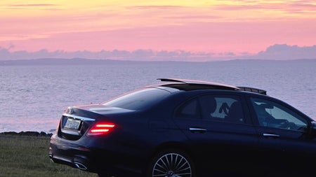 A luxury car parked at the coast with a sunset view