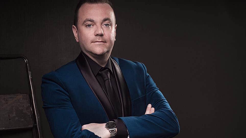 A man in dark jacket and shirt with arms crossed.