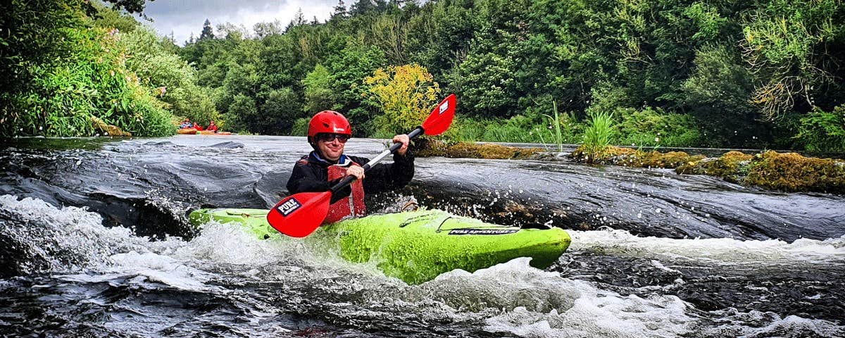 A lone kayaker rushing down small rapids on a river surrounded by trees