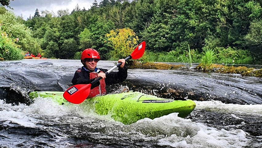 A lone kayaker rushing down small rapids on a river surrounded by trees