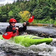 A lone kayaker rushing down small rapids on a river surrounded by trees