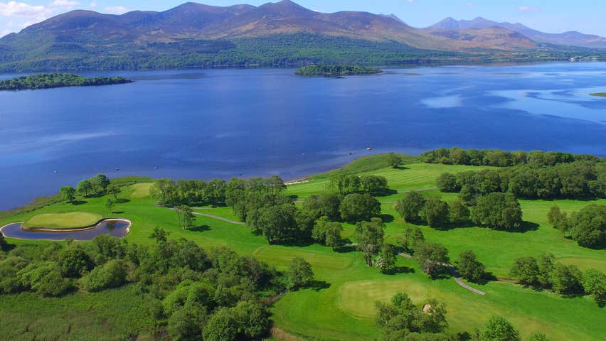 A view of a golf course by a lake with mountains in the background