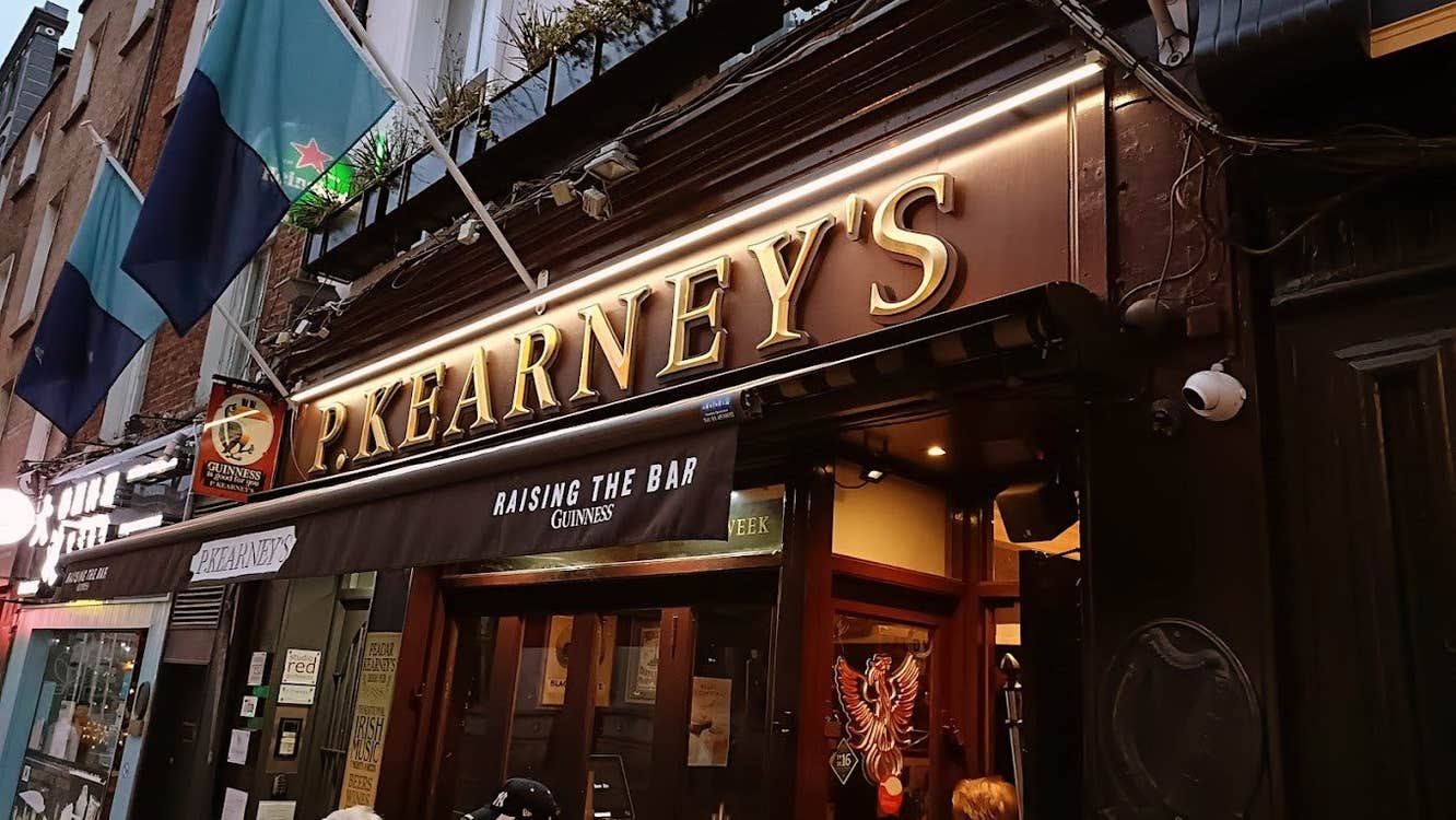 Outside of pub at dusk with two flags above a sign that reads P Kearneys