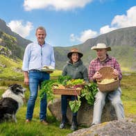 Three people posing with food in baskets and a sheepdog with a mountain in the background