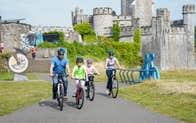Two adults and two children cycling in front of a castle