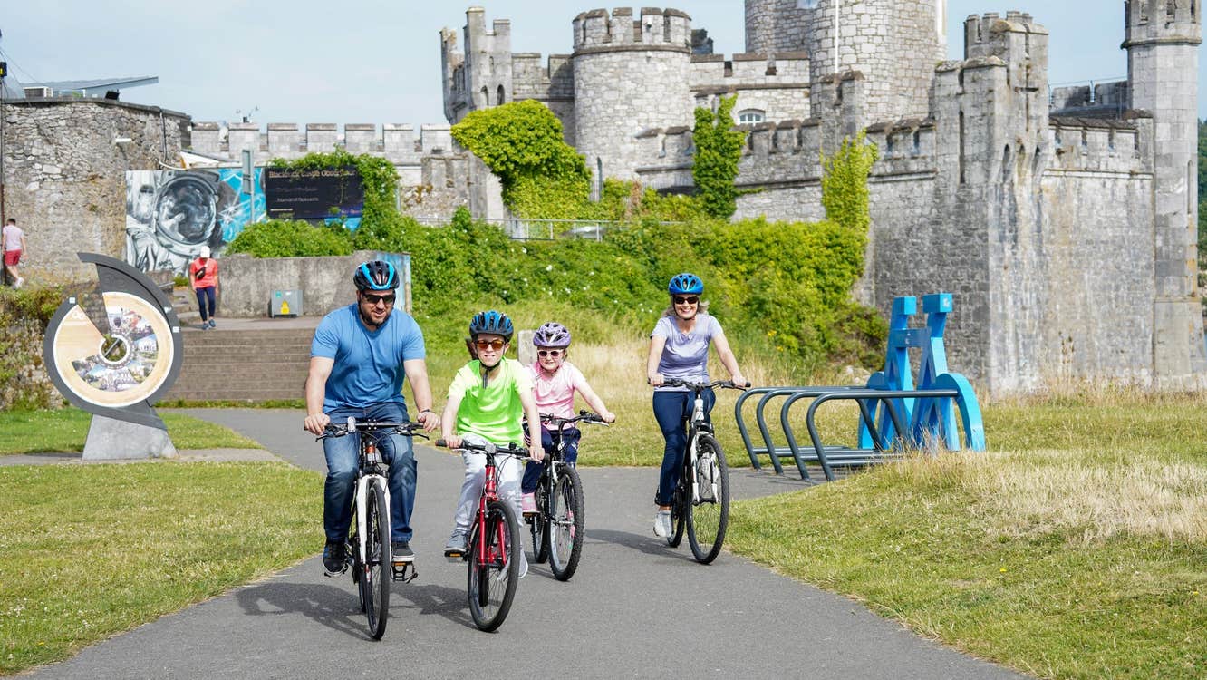 Two adults and two children cycling in front of a castle