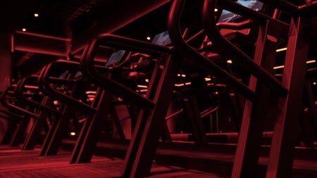 A dark red lit treadmill studio with rows of high performance machines
