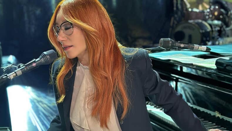 A woman with eyes closed is playing 2 keyboards and singing into a mic.