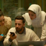 Several people are gathered around someone holding a mobile phone. They all look concerned.