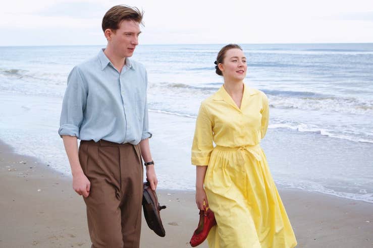 A scene from the movie Brooklyn, featuring a couple, male and female walking along the beach.