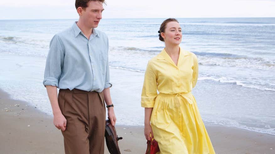 A scene from the movie Brooklyn, featuring a couple, male and female walking along the beach.