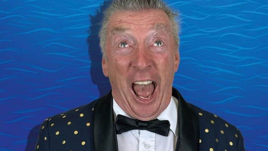 A man is appearing to shout with eyes looking upwards, wearing black jacket with small gold dots and black bow tie against blue wavy background.