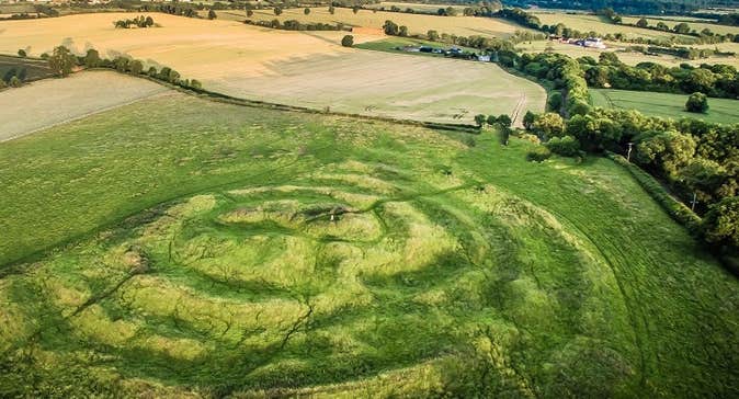 A large green field viewed from above with circular mounds visible as lighter shade of green.