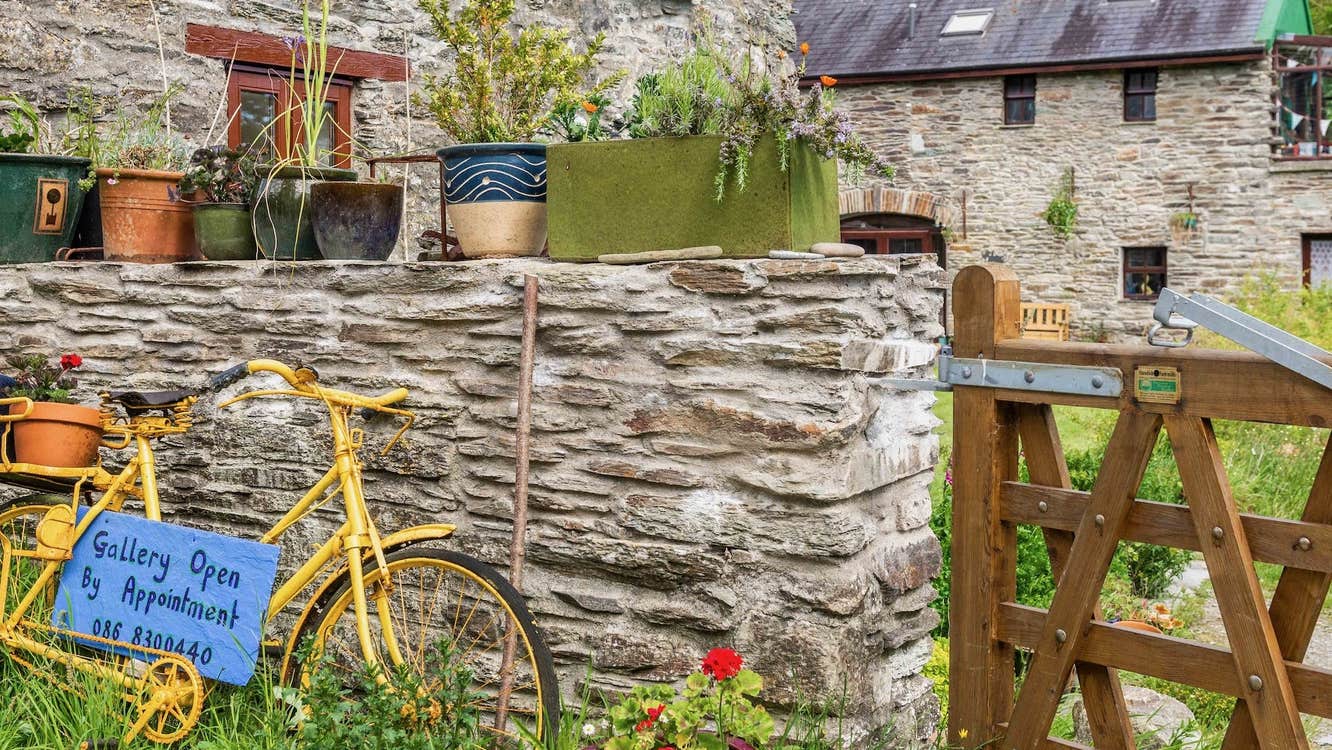 Yellow bike leaning against a stone wall next to a wooden gate with flower pots all around