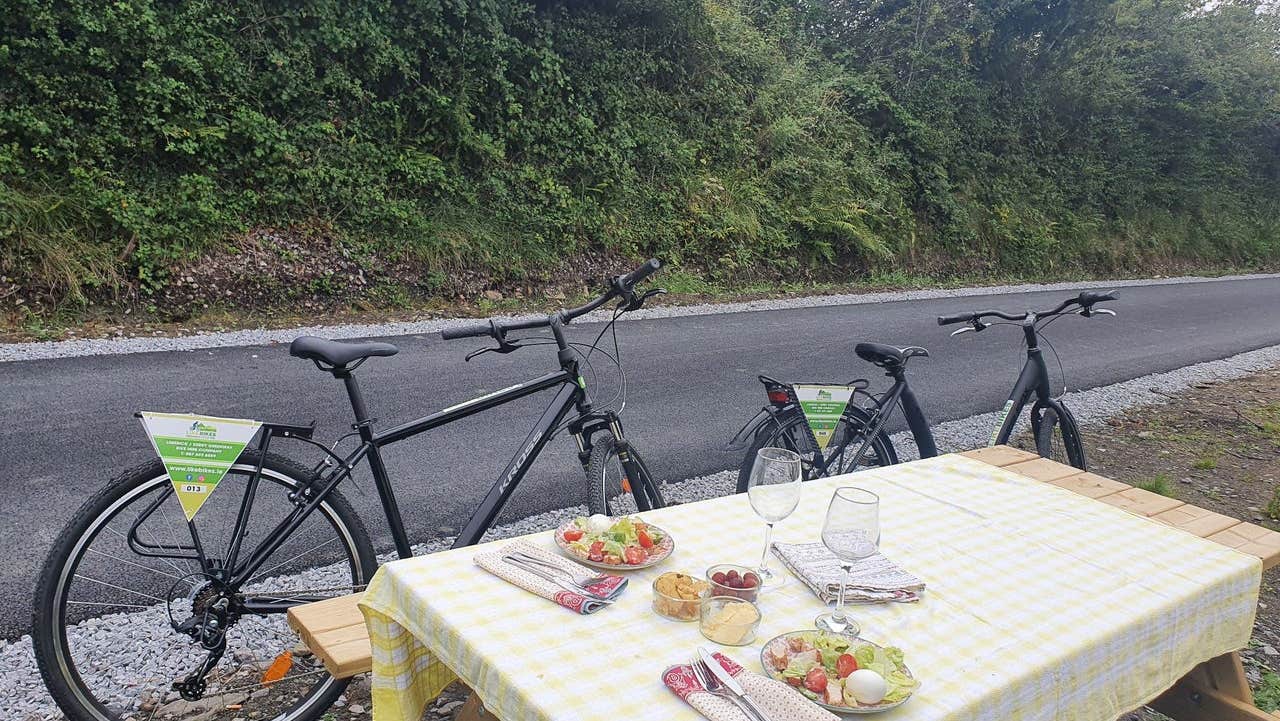 Two bikes parked by a picnic table with food and wine glasses