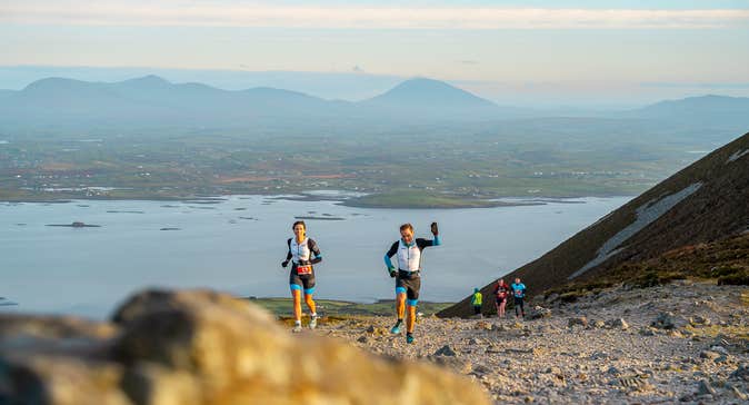 2 runners seen on a small rocky area with views of hills in the background.