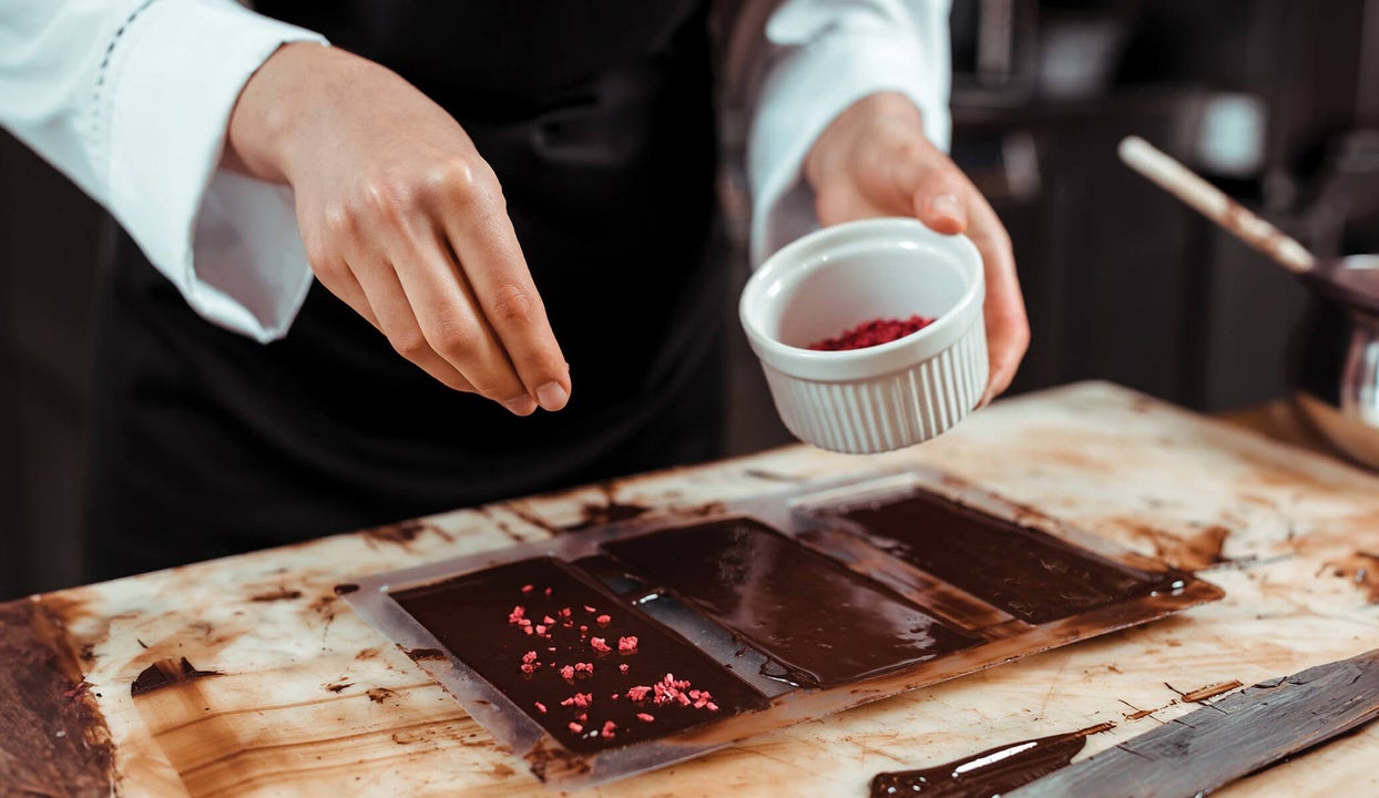 Someone in a chef uniform sprinkling flakes of nuts on chocolate squares