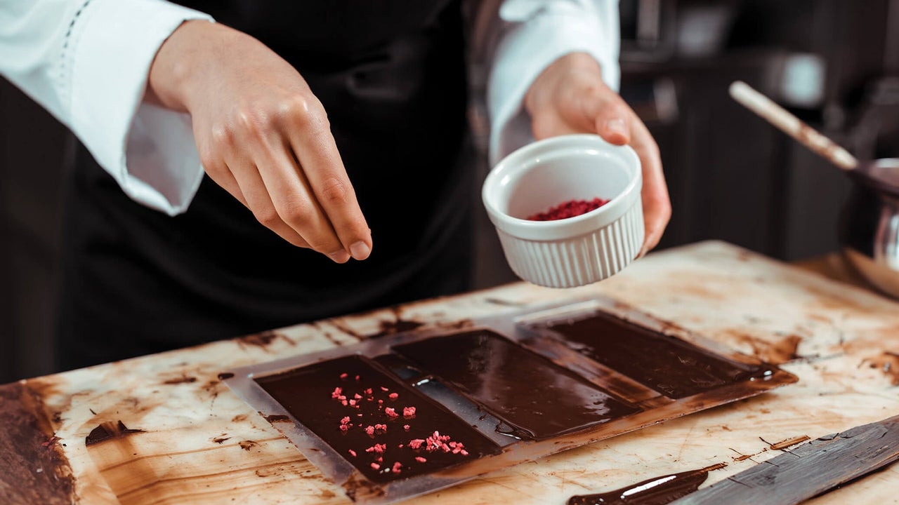Someone in a chef uniform sprinkling flakes of nuts on chocolate squares