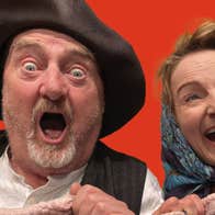 Close up head and shoulders shot of Jon Kenny wearing a hat with a shocked look on his face and Norma Sheahan, wearing a headscarf tied under her chin, laughing both clutching a blanket. 