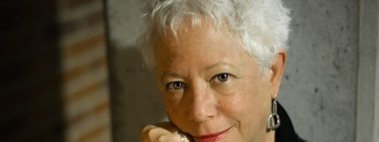 A woman smiling gently is resting her chin on her right hand.