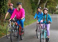 Two adults and two children on bicycles cycling along a greenway