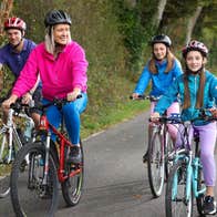 Two adults and two children on bicycles cycling along a greenway