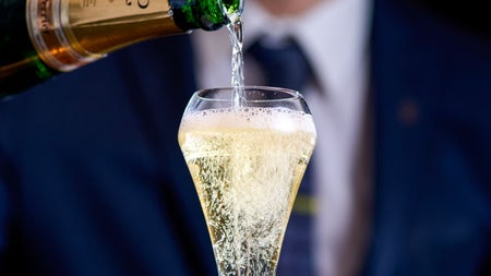 Champagne being poured into a tall glass by a person in formal attire