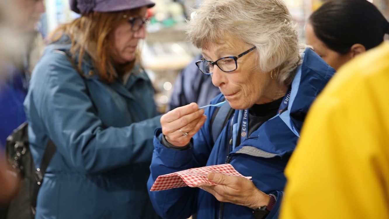 Person holding a small plastic spoon sampling food from a red and white napkin