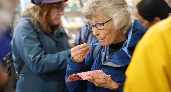 Person holding a small plastic spoon sampling food from a red and white napkin