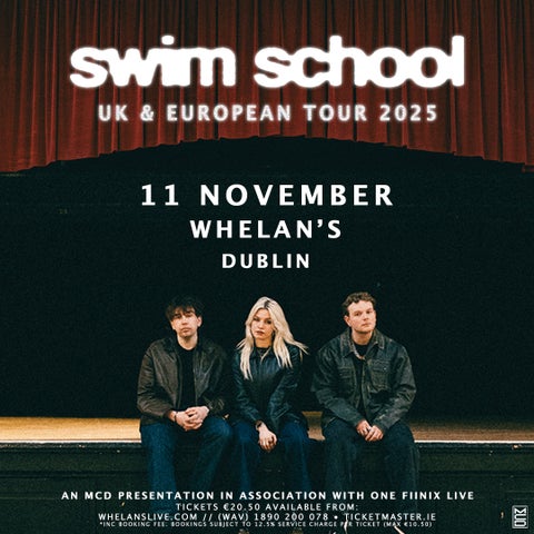 3 people dressed in black clothes and jackets are seated on the edge of a wooden stage.