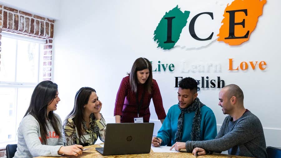 Four students and a teacher in a study group beneath the logo of the language school