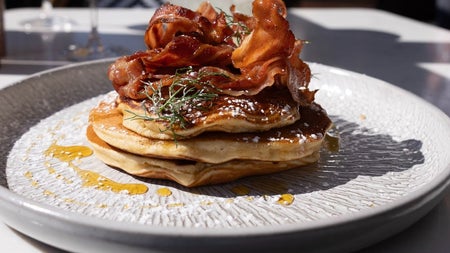 A close up of a plate with pancakes topped with bacon and syrup