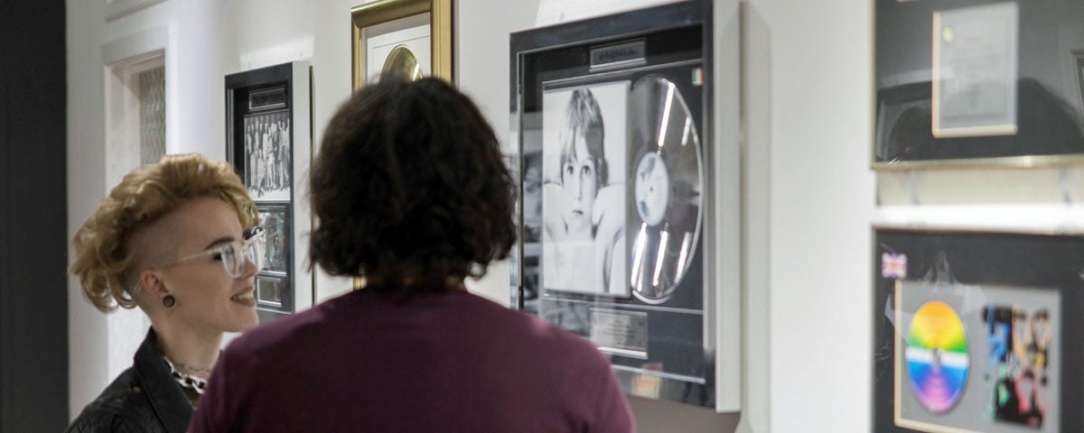 Image of two people viewing an assortment of platinum discs on the wall of fame