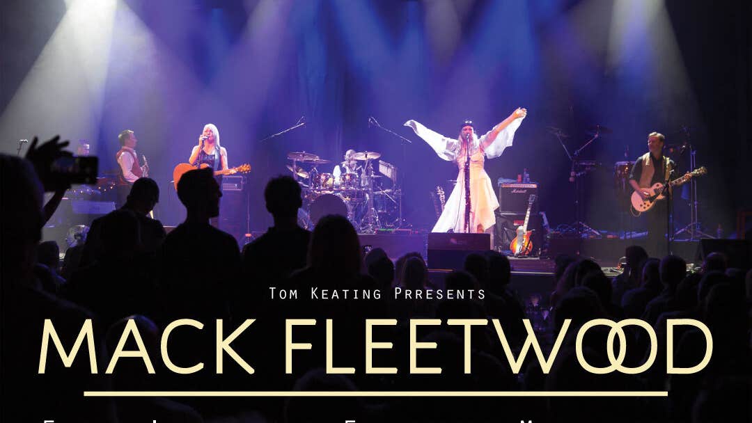 Distant view of a stage, with person dressed in white with arms outstretched and other band members, lit from above by many downward spotlights