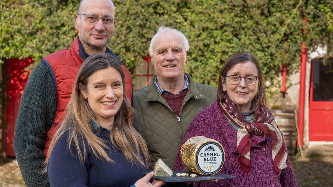 Four people smiling with one person holding a slate with cheese on it