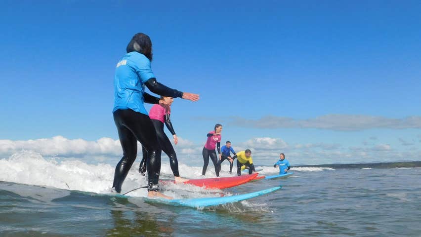 Kids on surf boards taking surfing lessons with an instructor in shallow waters