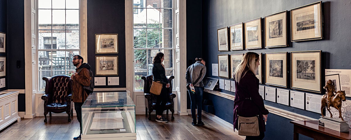 People looking at framed pictures on the wall inside The Little Museum of Dublin