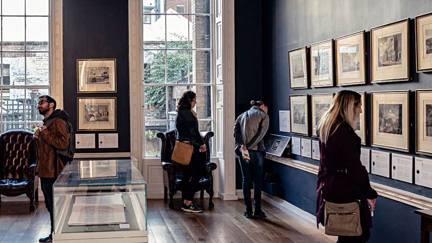 People looking at framed pictures on the wall inside The Little Museum of Dublin